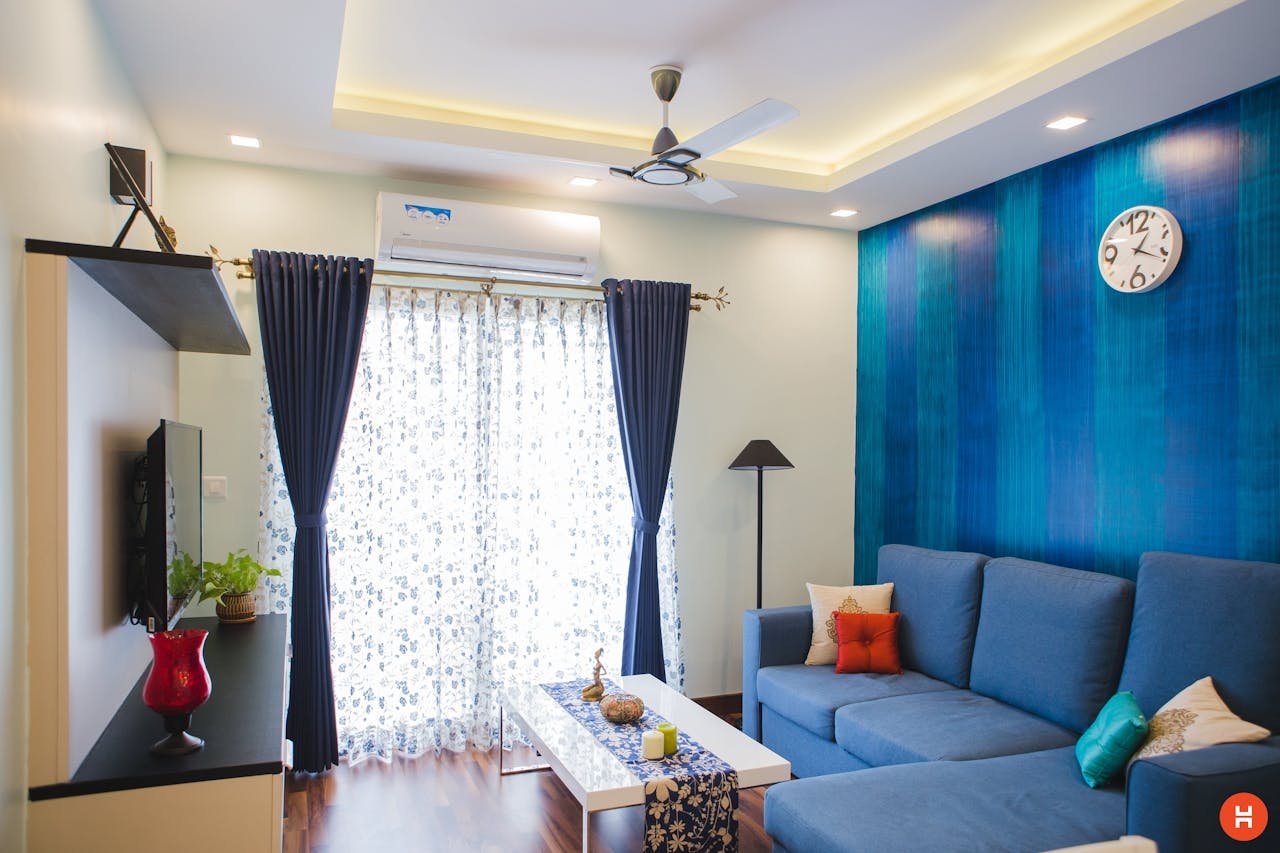 who-we-are Modern living room with blue accents, featuring a sofa, wall clock, and natural light.